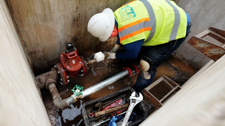 Water utility technician working on a smart meter and pipe system below ground